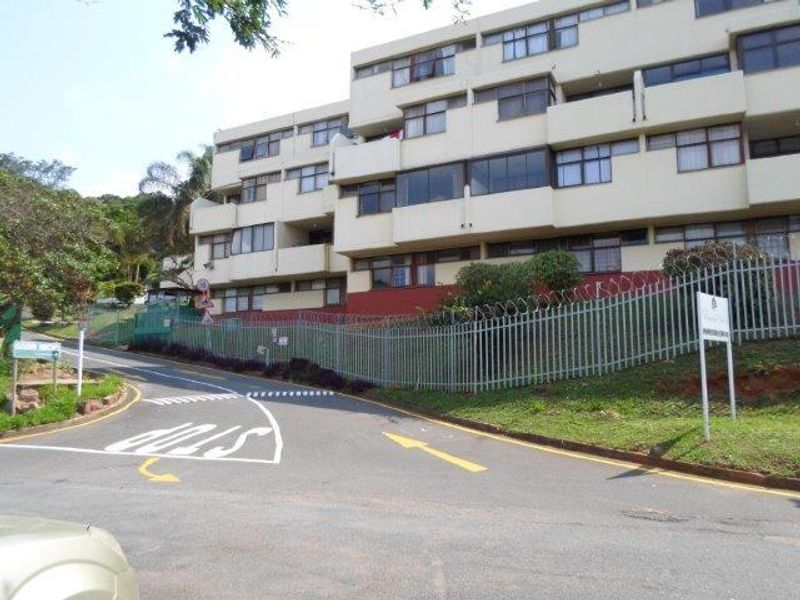 Exterior view of a multi-story apartment complex featuring a paved driveway, steel palisade fencing, and security razor wire.