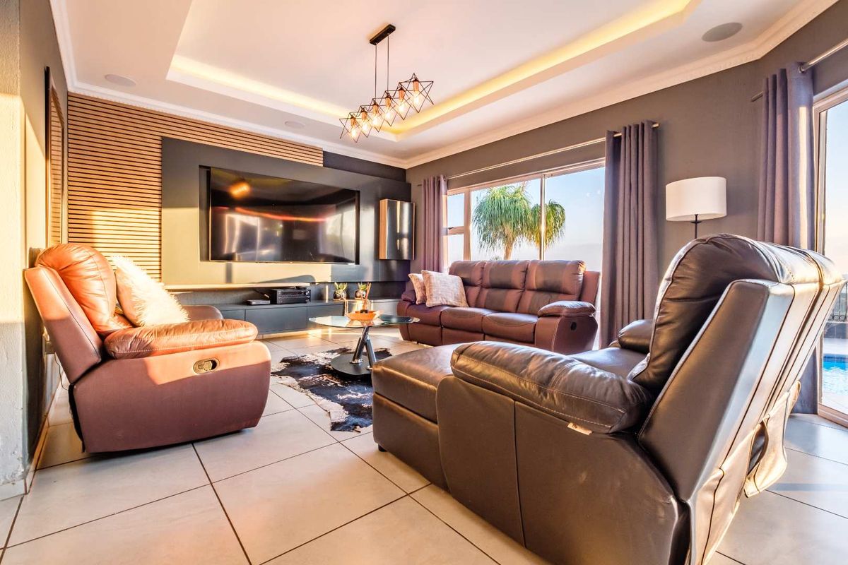 Modern living room featuring a recessed ceiling with cove lighting, stylish slatted timber wall paneling, tiled floors, and large sliding doors leading to the outdoors.