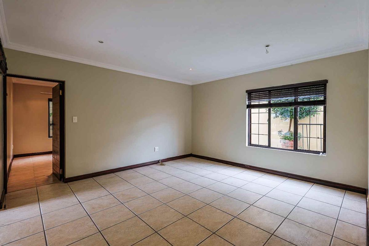 A spacious, empty bedroom featuring neutral wall paint, tiled flooring, and a window with fitted blinds, offering a blank canvas for personalization.