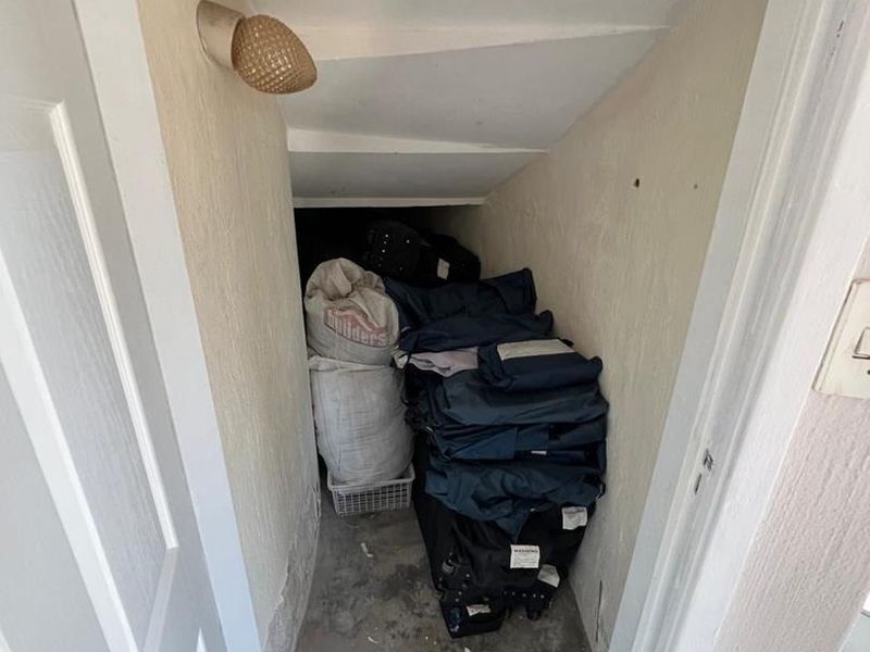 A small under-stair utility or storage space featuring a wall-mounted light fixture and unfinished wall and floor surfaces.