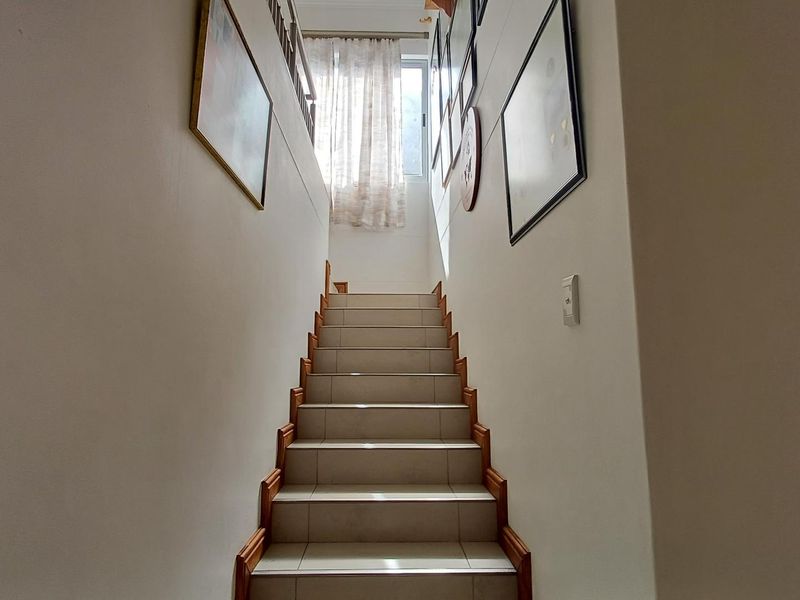 A bright, tiled staircase with wooden trim leading to an upper level, featuring a clean, neutral aesthetic.