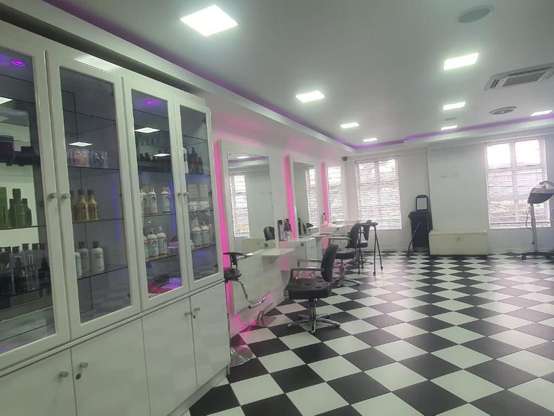 A well-maintained commercial salon space featuring checkered flooring, built-in display cabinetry, wall-mounted mirrors, and modern recessed lighting.