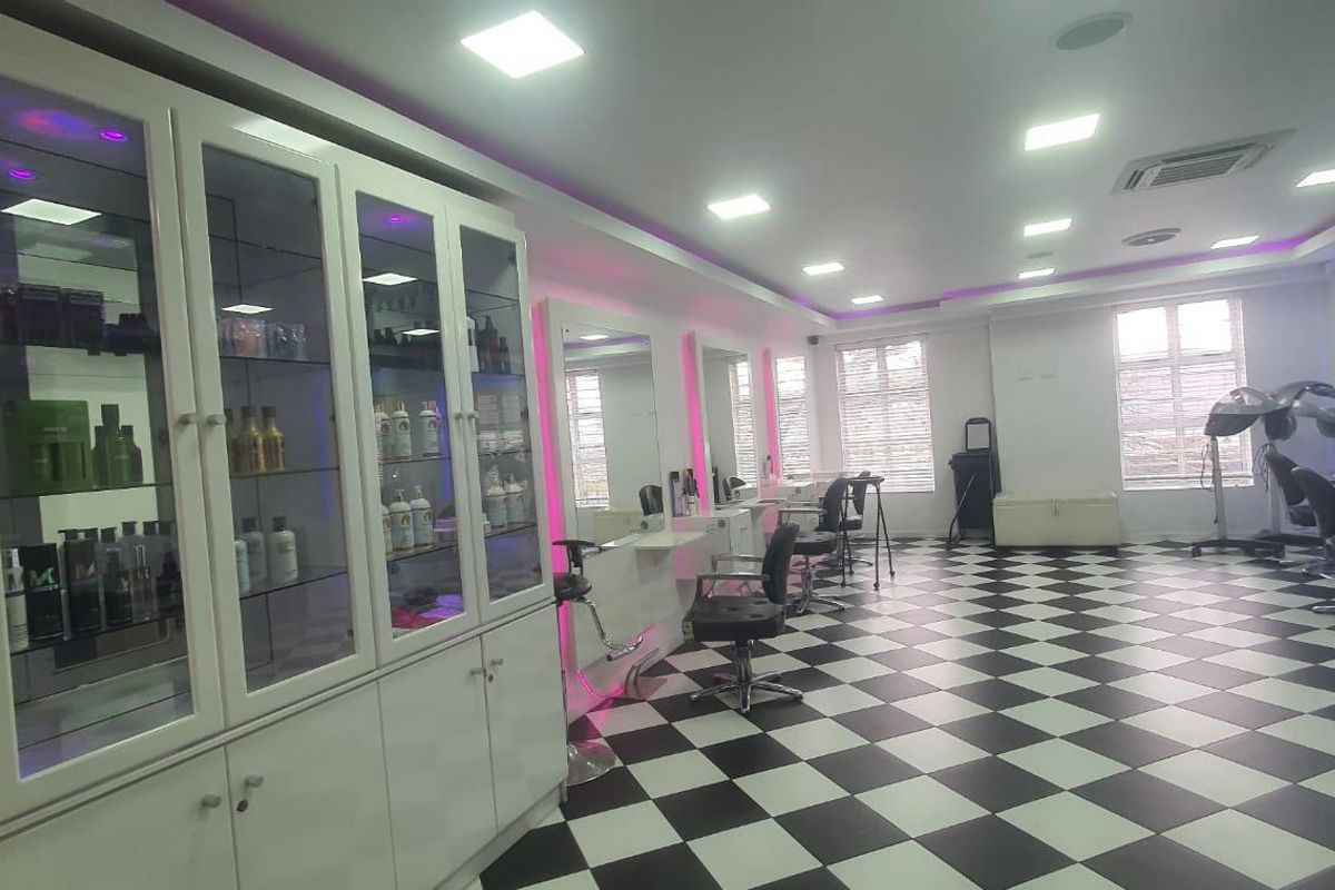 A well-maintained commercial salon space featuring checkered flooring, built-in display cabinetry, wall-mounted mirrors, and modern recessed lighting.