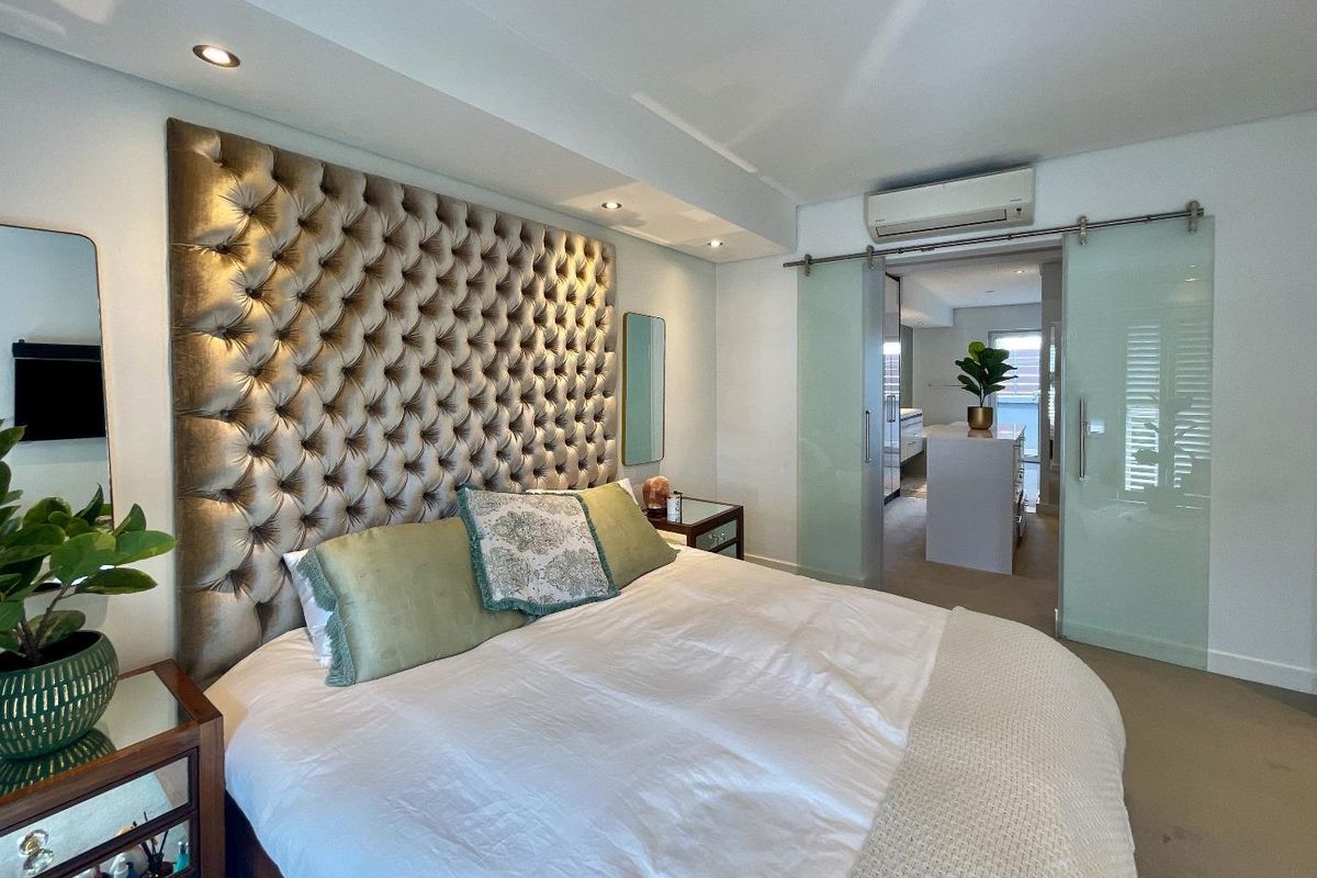 A well-maintained bedroom featuring a tufted headboard, recessed ceiling lighting, and sliding glass doors leading to an adjoining bathroom area.