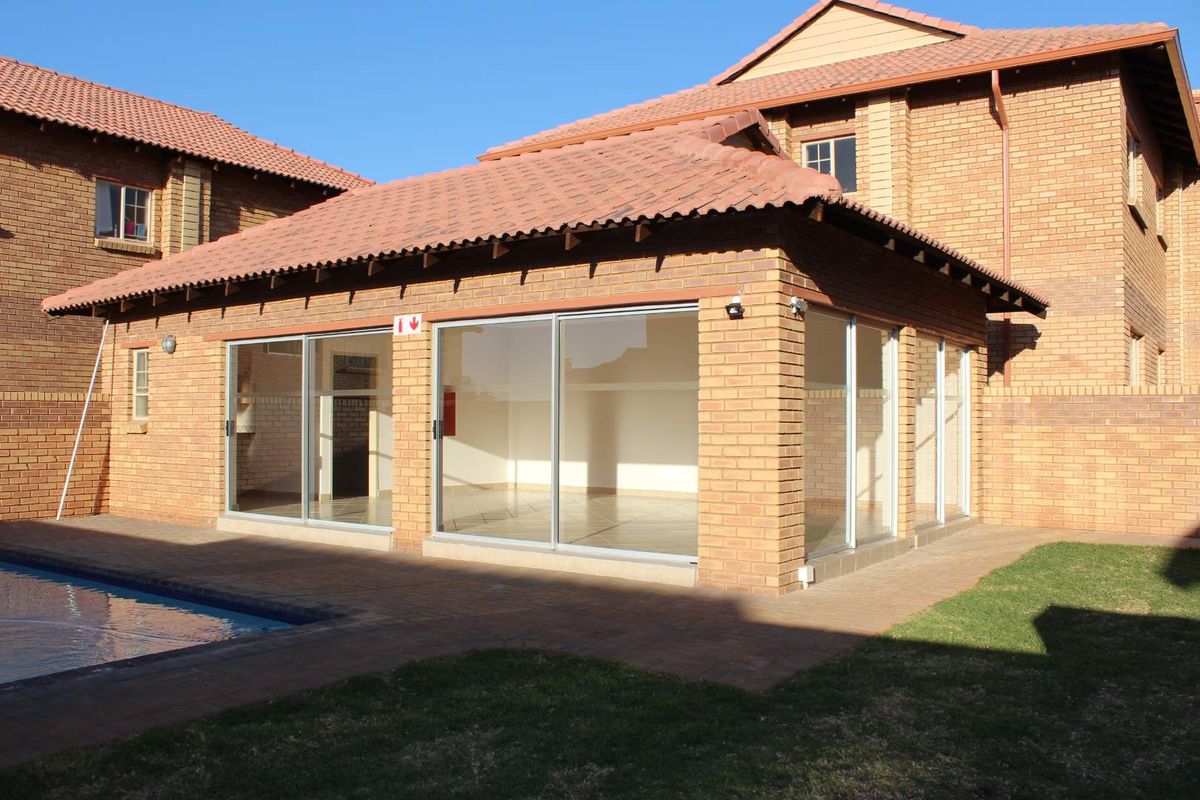 Rear view of the apartment featuring a brick facade, tiled roof, large sliding glass doors, a paved patio area, and a swimming pool.
