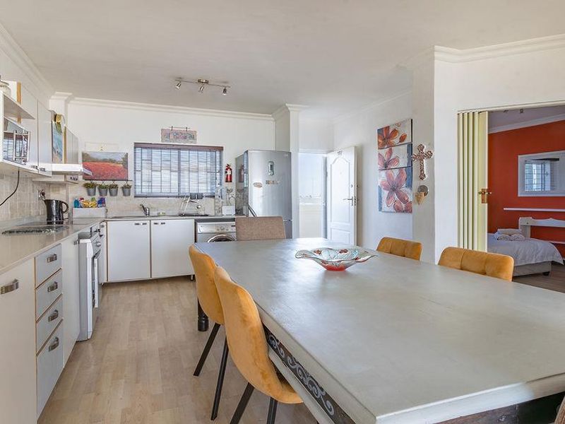 Open-plan kitchen and dining area featuring laminate flooring, white cabinetry, and a functional layout with direct access to an adjacent bedroom.