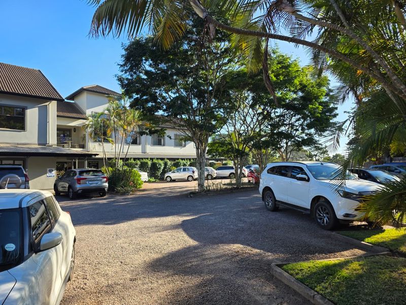 Exterior view of a multi-story commercial building featuring a paved parking area, mature trees, and well-maintained landscaping.