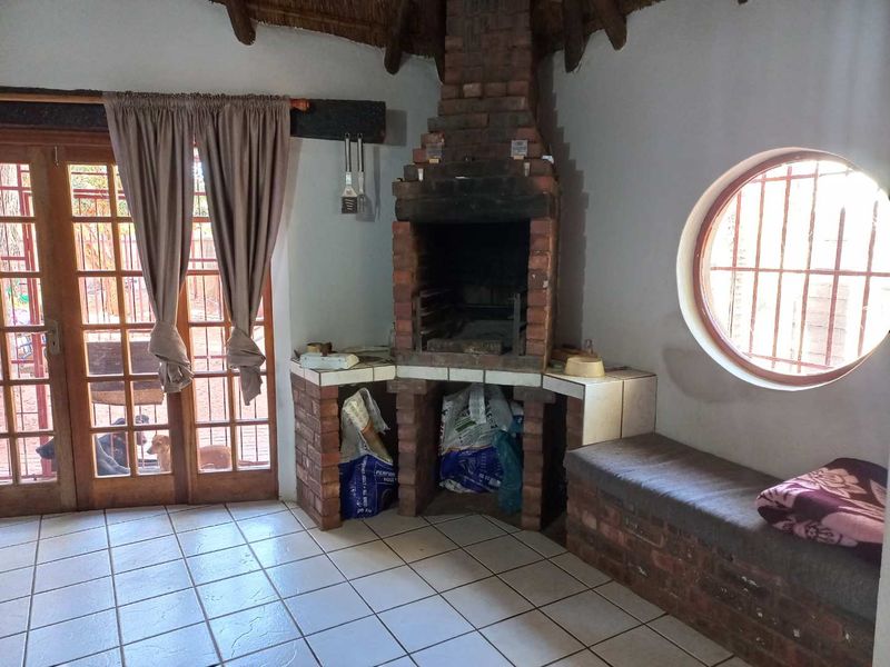 Covered patio area featuring a built-in brick braai, tiled flooring, and a unique circular window with security bars.