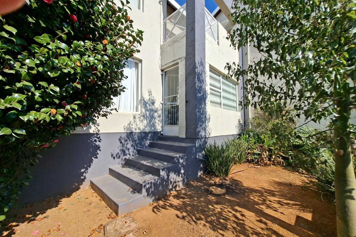 Rear exterior view of the townhouse featuring concrete stairs leading to an entrance, a balcony with metal railings, and surrounding garden area.