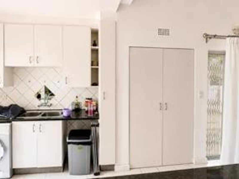 Functional kitchen area featuring white cabinetry, tiled backsplash, double sink, and integrated laundry space with direct access to the patio.