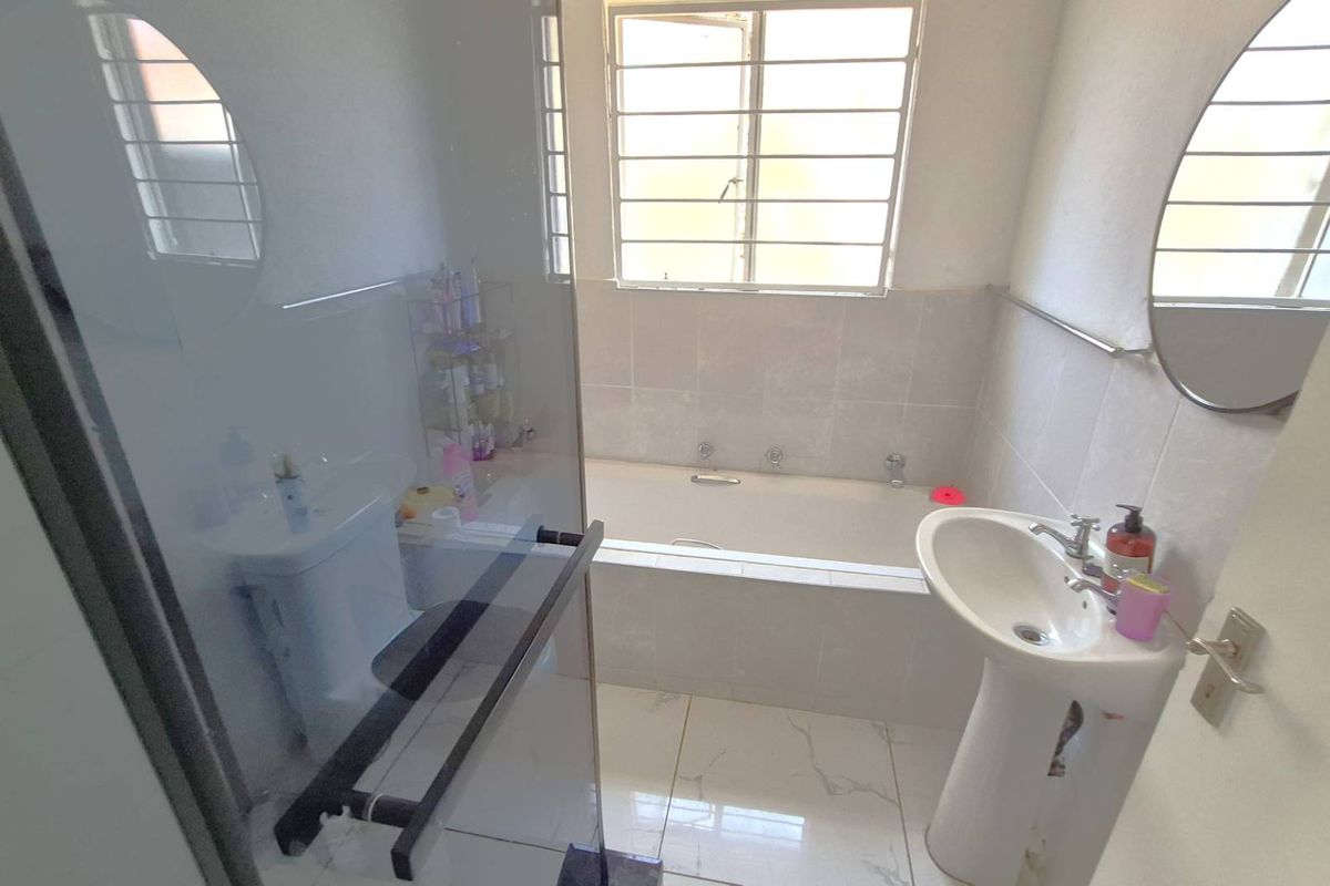 A functional bathroom featuring a pedestal sink, a built-in bathtub with tiled surround, and a window with security bars.