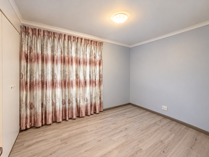 A clean, empty bedroom featuring light-toned laminate flooring, neutral walls, and a built-in wardrobe with sliding doors.