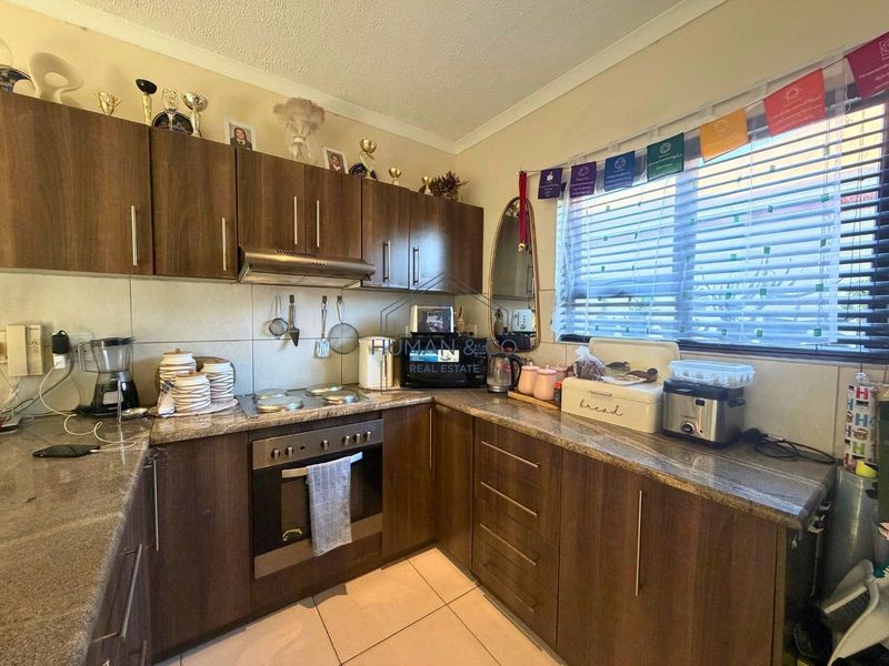 Functional kitchen featuring dark wood-look cabinetry, granite countertops, built-in oven, and electric hob with a tiled backsplash and flooring.