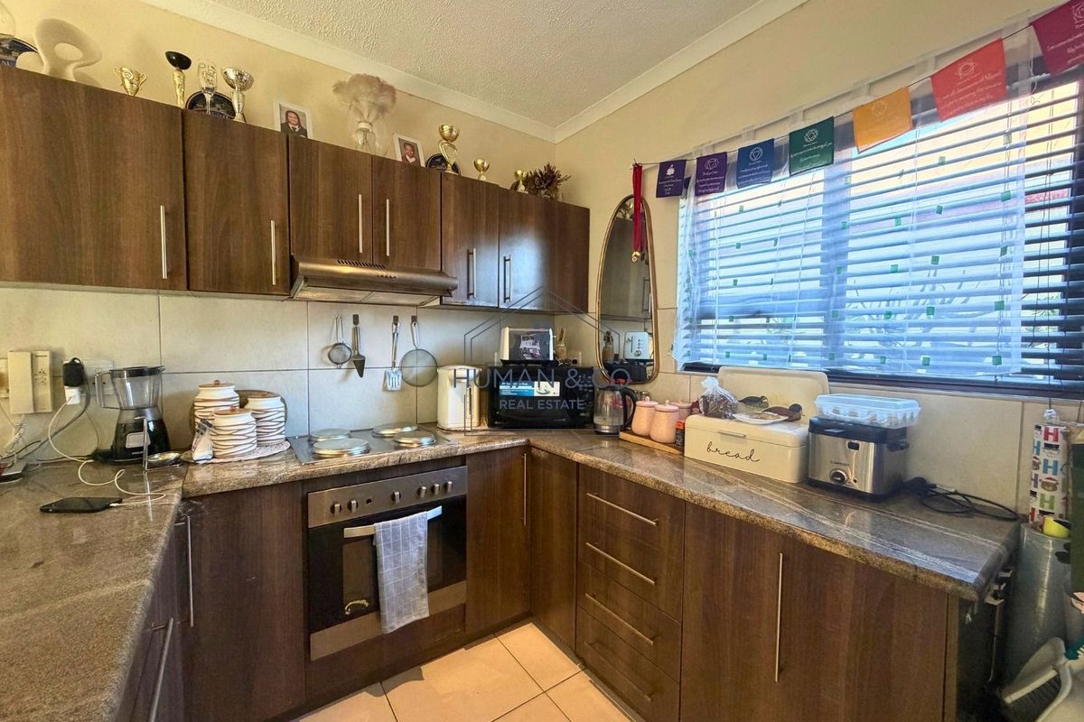 Functional kitchen featuring dark wood-look cabinetry, granite countertops, built-in oven, and electric hob with a tiled backsplash and flooring.