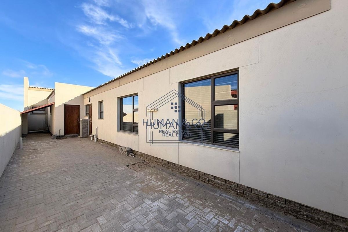 Rear exterior view of the property featuring paved courtyard area, aluminium window frames, and access doors.