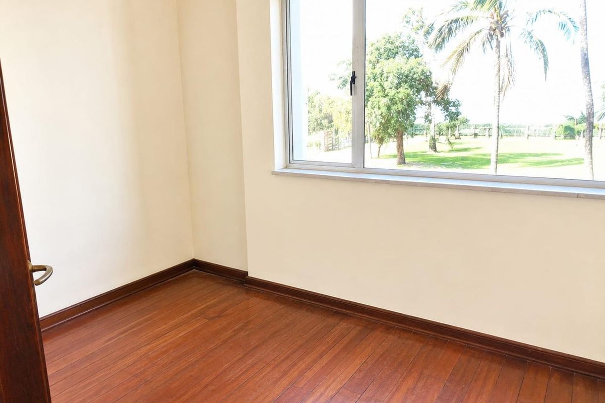 An empty bedroom featuring polished hardwood flooring, neutral walls, and a large window with views of the surrounding greenery.