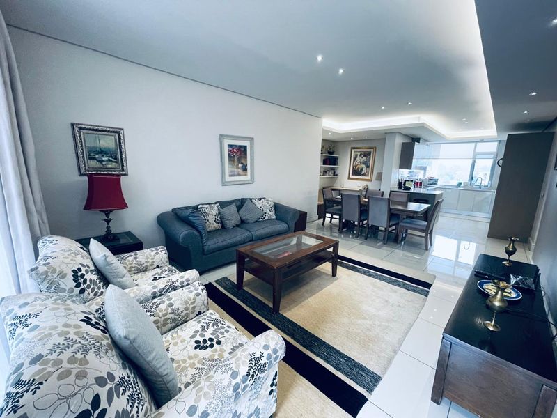 Spacious open-plan living and dining area featuring modern recessed lighting, sleek porcelain floor tiles, and a seamless transition into a contemporary kitchen space.