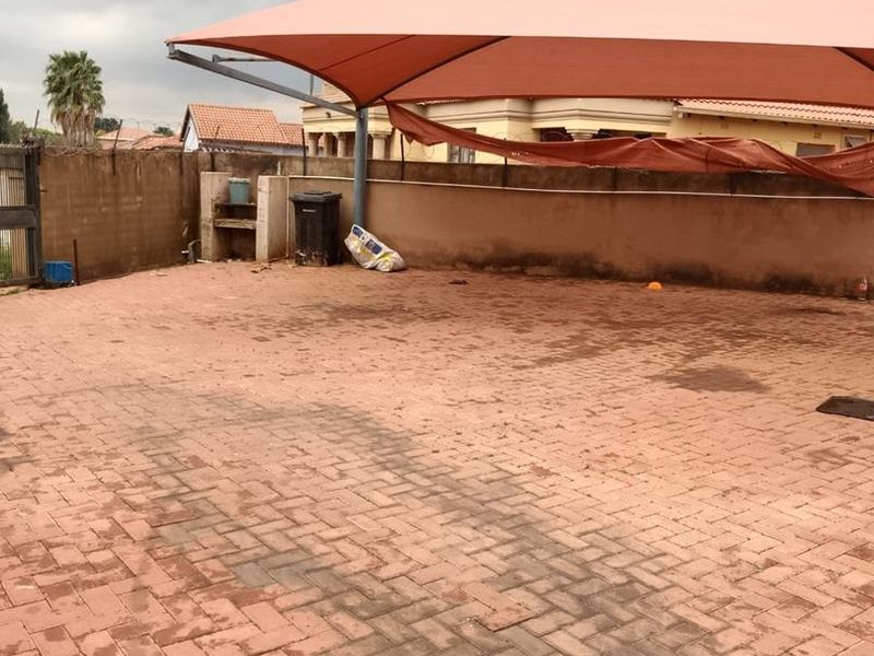 Outdoor paved patio area featuring a large shade sail and a built-in braai, enclosed by a perimeter wall.