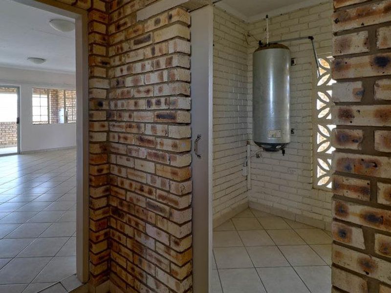 Utility area featuring exposed brickwork, ceramic floor tiles, and a wall-mounted electric water heater, providing functional space for laundry or storage needs.
