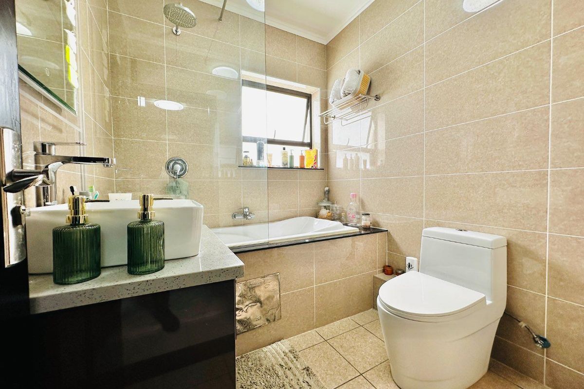 A compact, modern bathroom featuring a built-in bathtub with a glass shower screen, a wall-mounted toilet, and a vanity with a countertop basin.