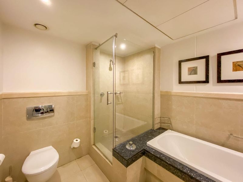 A well-maintained bathroom featuring a glass-enclosed shower, a built-in bathtub with a stone surround, and a wall-mounted toilet with neutral tiling.