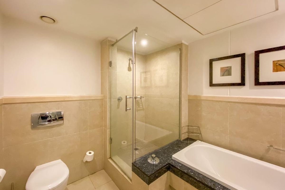 A well-maintained bathroom featuring a glass-enclosed shower, a built-in bathtub with a stone surround, and a wall-mounted toilet with neutral tiling.