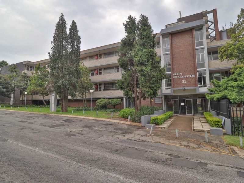 Front exterior view of the Klein Drakenstein apartment building, featuring a brick facade, secure entrance gate, and established communal garden area.