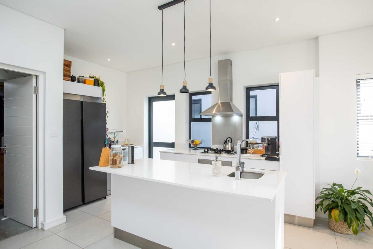 Modern kitchen featuring a central island with stone countertops, stainless steel extractor fan, gas hob, and sleek built-in cabinetry with recessed and pendant lighting.
