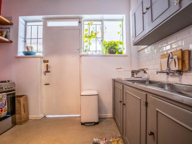 A functional kitchen featuring grey cabinetry, subway tile backsplash, stainless steel sink, and a freestanding stove with direct access to an exterior door.