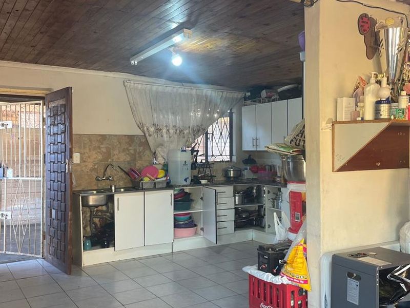 A functional kitchen area featuring tiled flooring, timber ceiling, and built-in cabinetry with an integrated sink, providing direct access to the exterior.