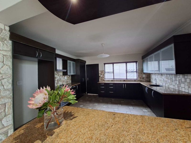 A spacious kitchen featuring dark cabinetry, granite countertops, tiled backsplash, and tiled flooring, offering a functional layout with ample storage space.