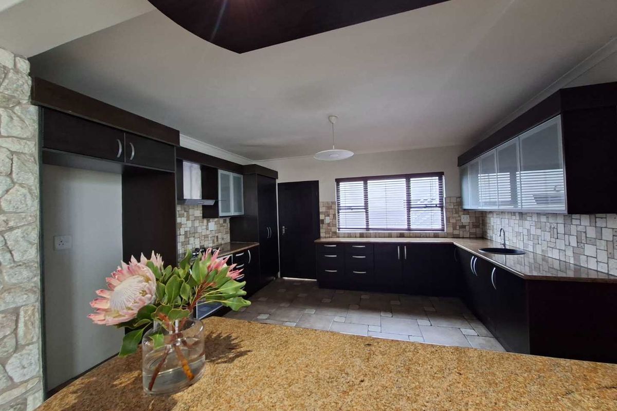 A spacious kitchen featuring dark cabinetry, granite countertops, tiled backsplash, and tiled flooring, offering a functional layout with ample storage space.