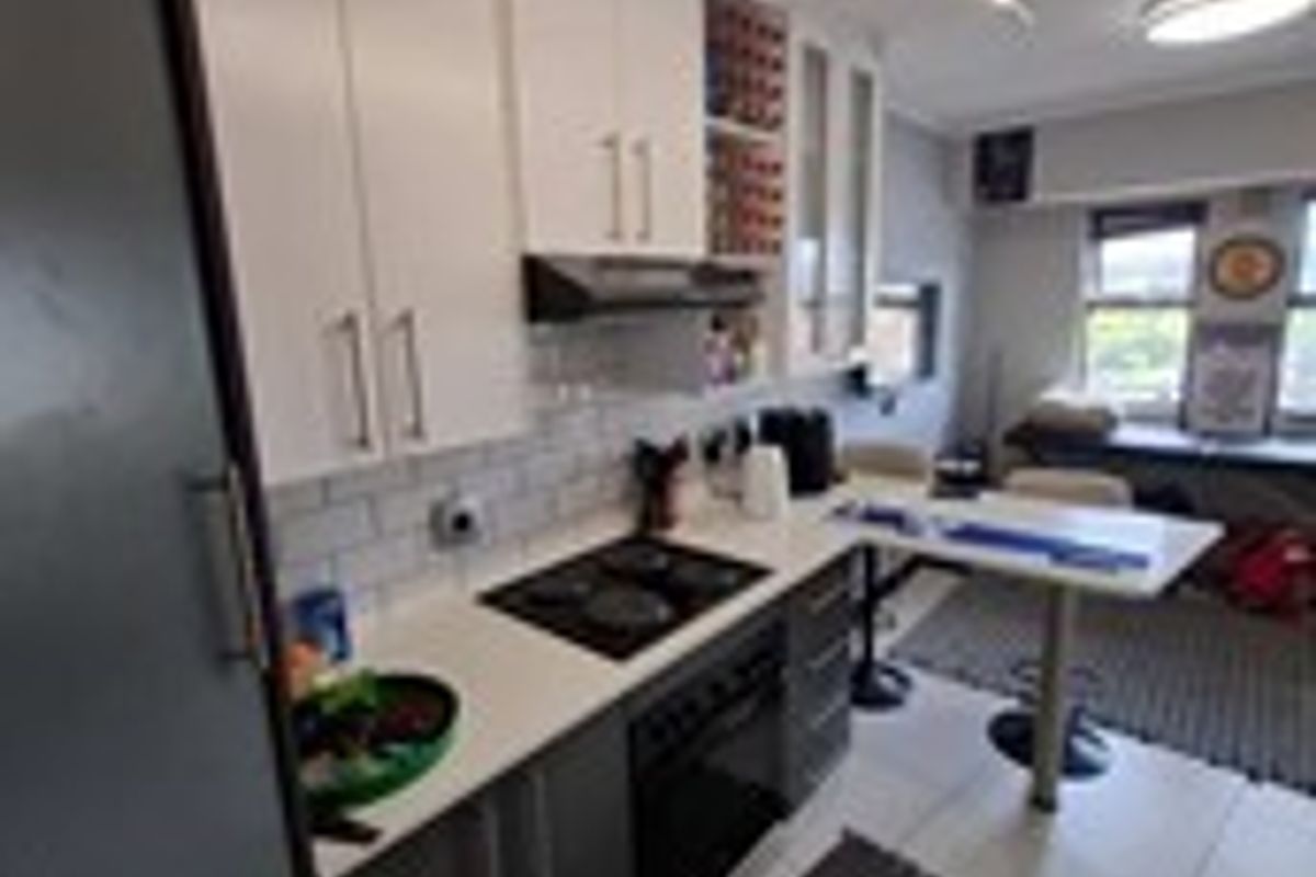 Modern kitchen featuring two-tone cabinetry, stone countertops, subway tile backsplash, integrated hob and oven, and a convenient breakfast bar area.