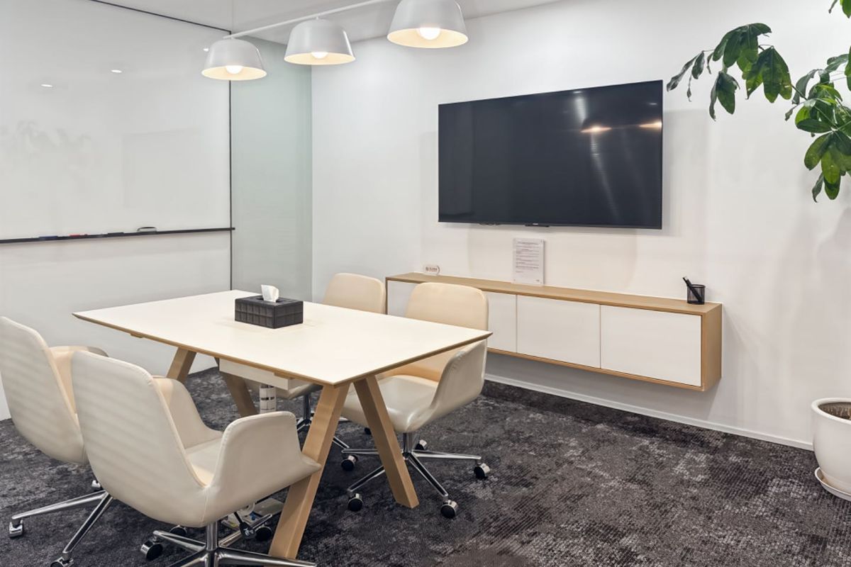 A modern, well-lit office meeting room featuring a glass whiteboard, wall-mounted storage cabinetry, and professional carpeted flooring.