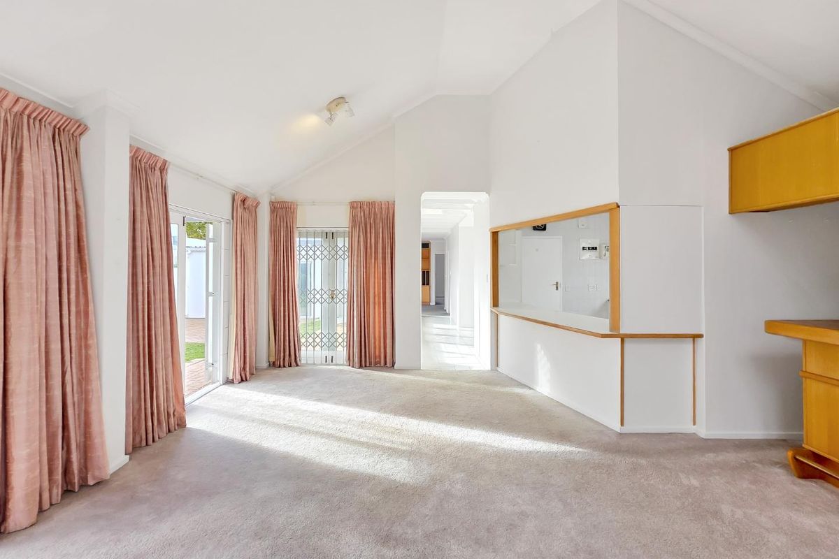 Spacious living area featuring a vaulted ceiling, neutral carpeting, and a convenient serving hatch connecting to the kitchen area.
