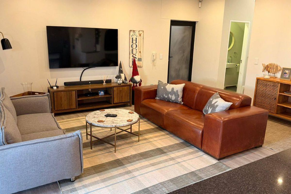 A comfortable living room featuring neutral flooring, recessed lighting, and a clear view into an adjacent bathroom area.