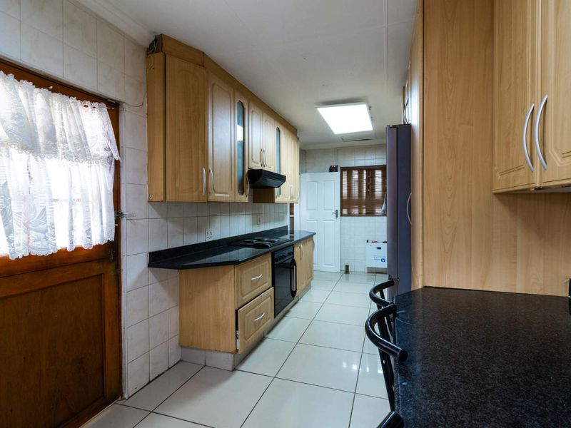 A functional kitchen featuring light wood cabinetry, dark granite countertops, tiled flooring, and a built-in oven with an extractor fan.
