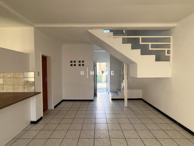 An open-plan living area featuring tiled flooring, a staircase with a metal balustrade, and a functional kitchen counter with a tiled backsplash.