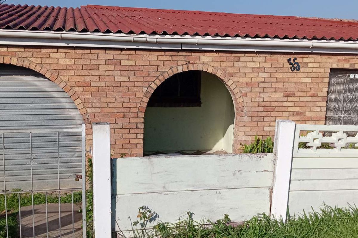 Front elevation of a single-story brick house featuring an arched entrance, roller shutter garage door, and a precast concrete boundary wall.