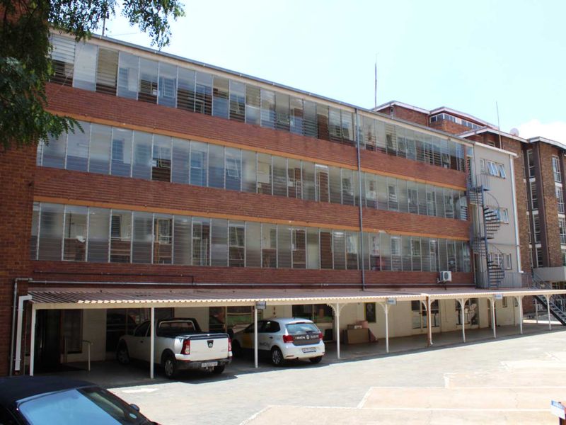 Exterior view of a multi-story apartment building featuring a brick facade, rows of louvre windows, and a covered carport area.
