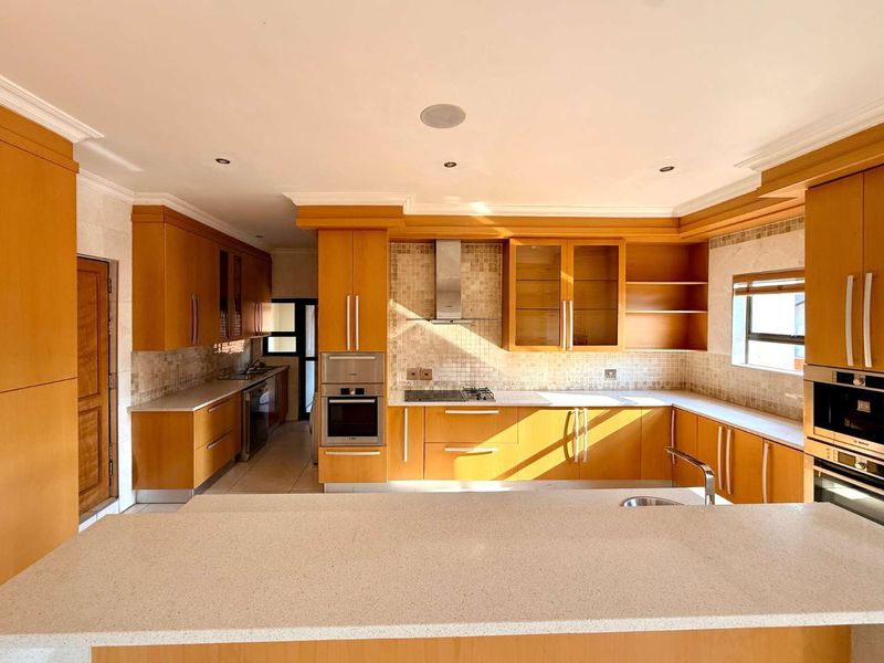 Spacious kitchen featuring warm-toned wooden cabinetry, stone countertops, a mosaic tile backsplash, and integrated stainless steel appliances including an oven and gas hob.