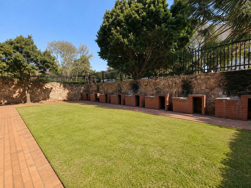 Communal garden area featuring a row of brick built-in braai stations, stone retaining walls, and well-maintained lawn space.