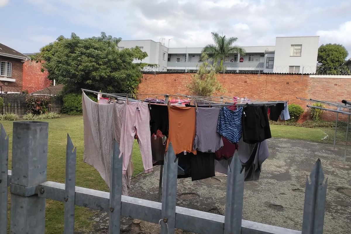 A communal outdoor area featuring a paved drying yard, lawn, and perimeter security fencing with brick boundary walls.