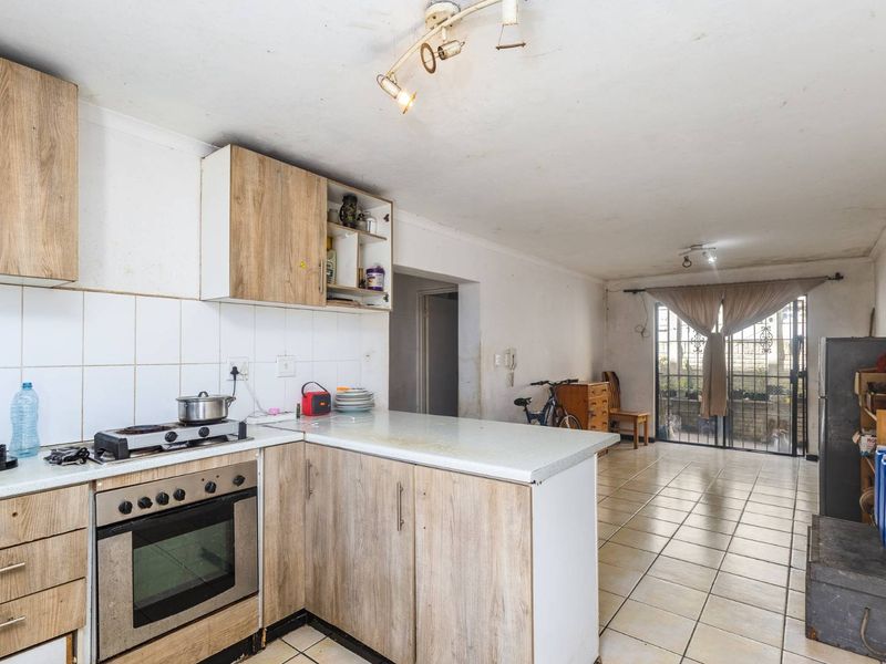 Open-plan kitchen and living area featuring wood-look cabinetry, gas hob, tiled flooring, and direct access to an outdoor space through a security gate.