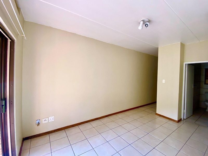 An empty, neutrally painted living area featuring tiled flooring, skirting boards, and a ceiling light fixture, providing a blank canvas for interior design.
