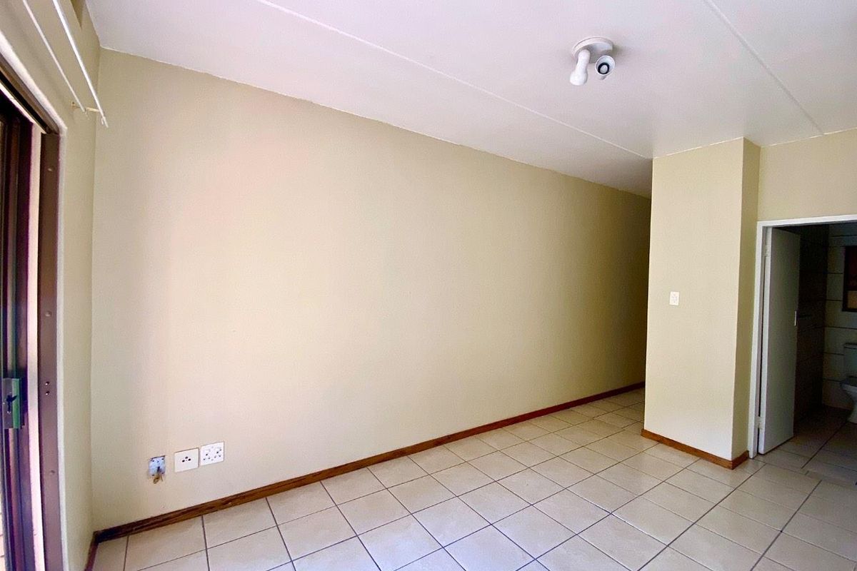 An empty, neutrally painted living area featuring tiled flooring, skirting boards, and a ceiling light fixture, providing a blank canvas for interior design.