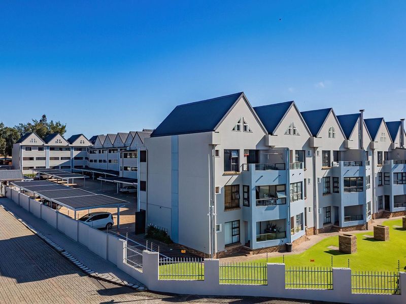 Aerial view of a multi-story apartment complex featuring metal roofing, covered parking facilities, and well-maintained landscaped grounds with perimeter fencing.