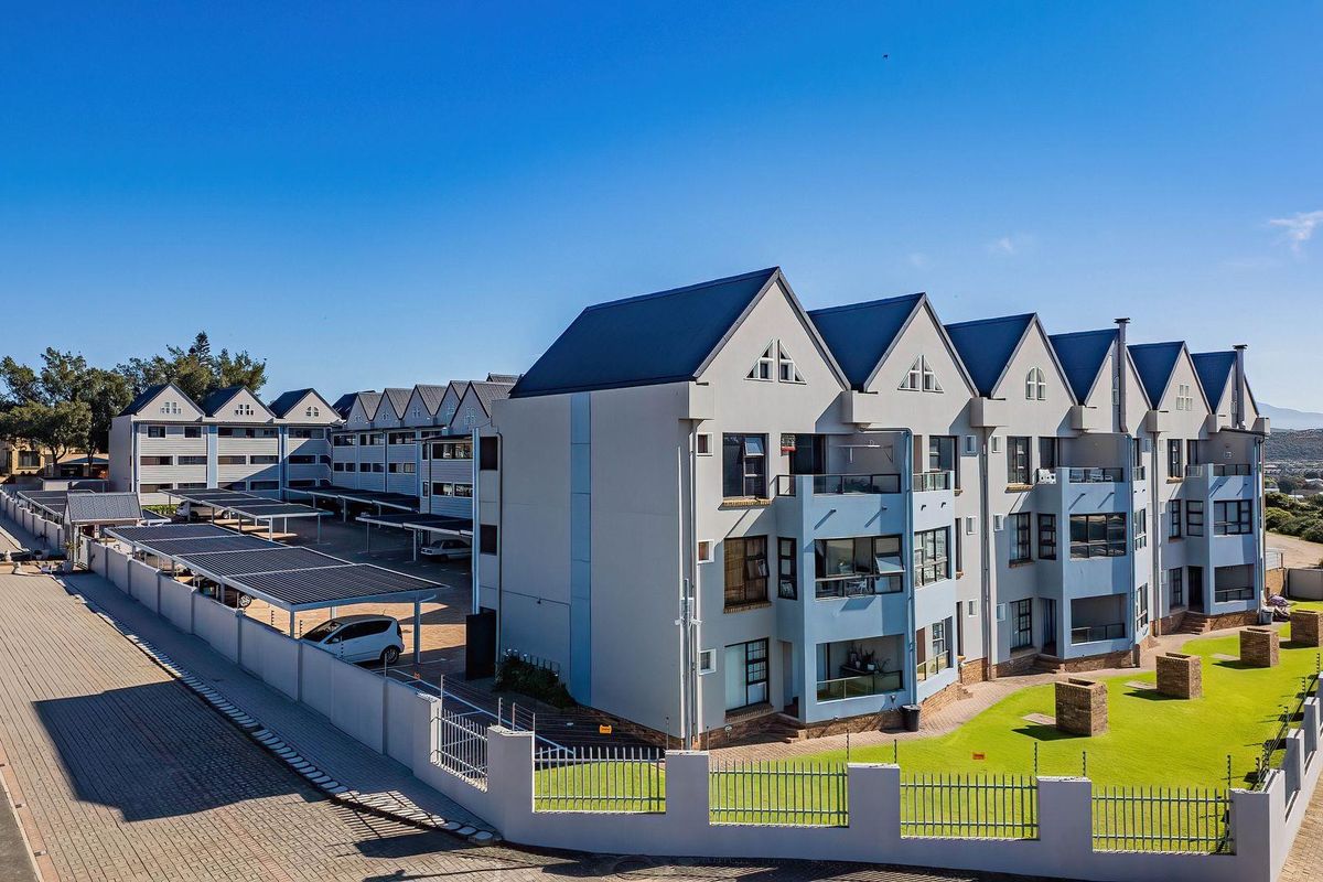 Aerial view of a multi-story apartment complex featuring metal roofing, covered parking facilities, and well-maintained landscaped grounds with perimeter fencing.