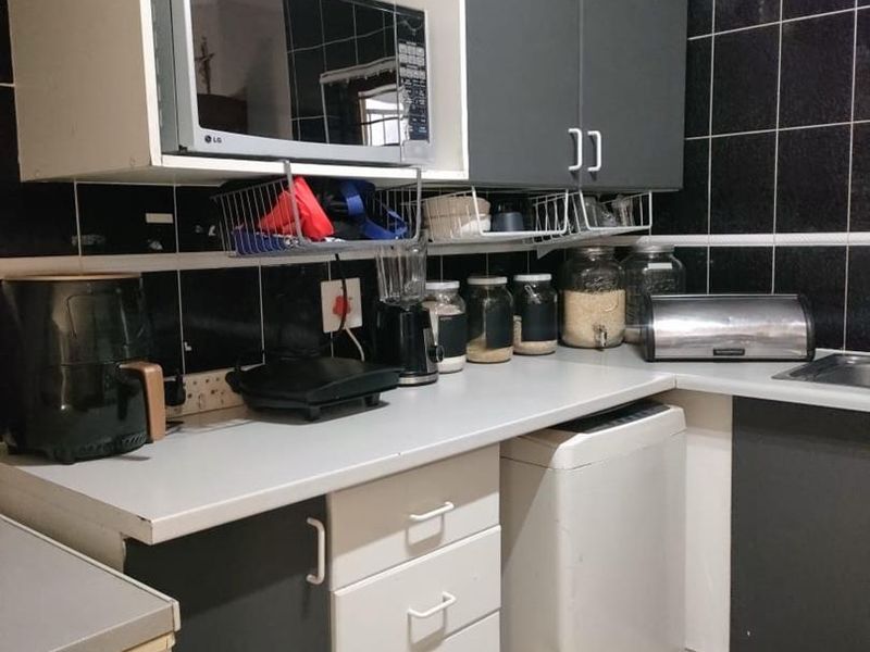 A compact kitchen featuring dark tiled walls, laminate countertops, and a mix of white and grey cabinetry with built-in storage solutions.