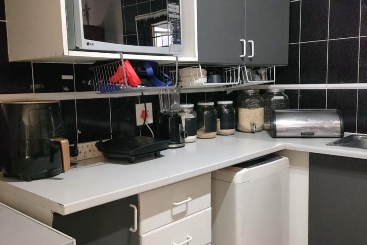 A compact kitchen featuring dark tiled walls, laminate countertops, and a mix of white and grey cabinetry with built-in storage solutions.
